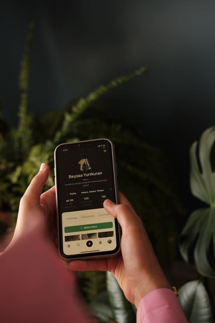 Close-up of hands holding a smartphone with app interface amidst green plants.