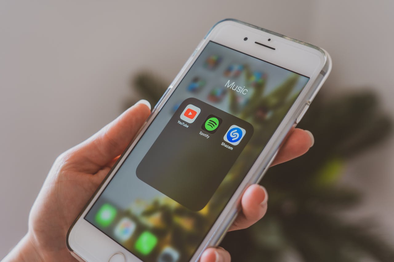 hero-img-02 Hand holding a smartphone displaying popular music apps like Spotify and Shazam in a close-up shot.