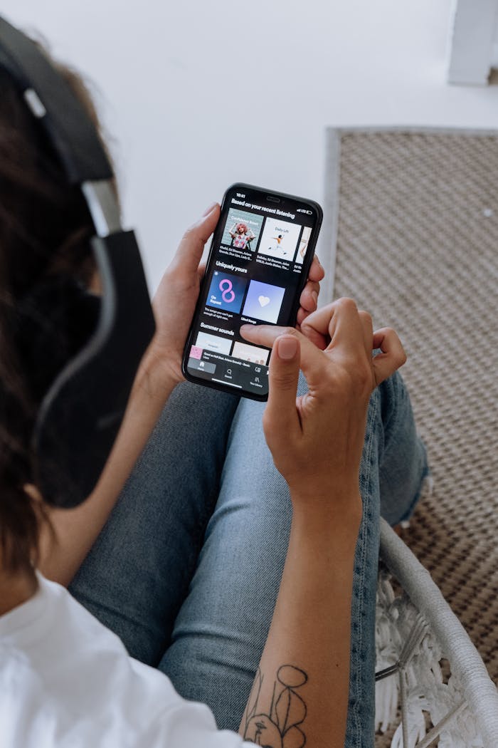 A close-up of a person relaxing indoors, using a smartphone and headphones to enjoy music.